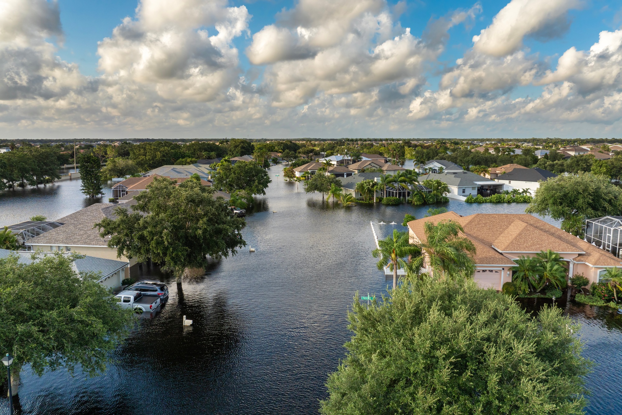 Aerial view of a residential neighborhood in Florida submerged in floodwater, illustrating Florida Flood Zone Impact with houses partially underwater and cars surrounded by water.
