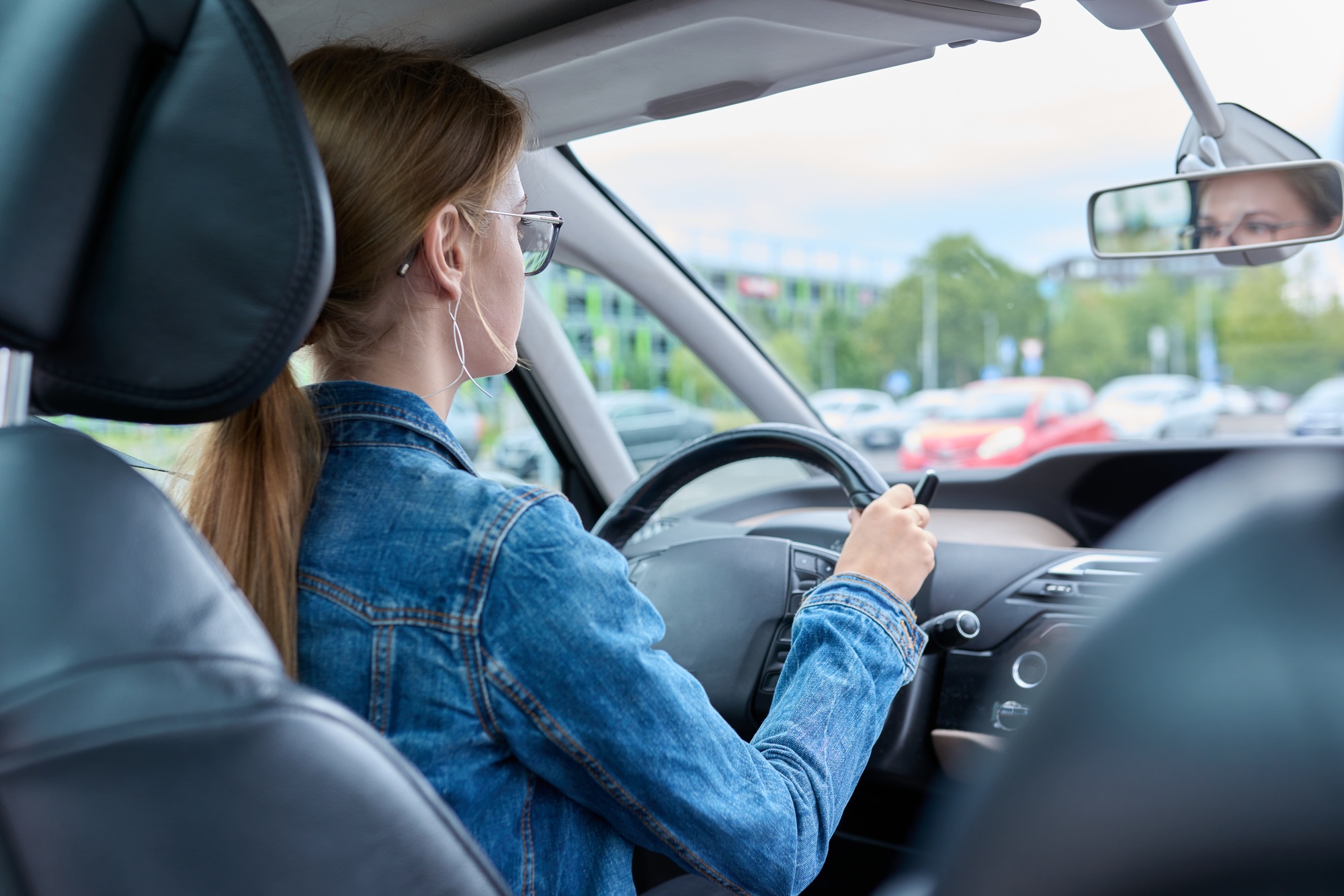 Teenage girl driver in glasses sitting behind wheel of car